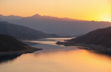 Naklejka premium Tranquil panoramic photo of Negratin reservoir in Spain at sunset. Golden sun illuminates sky, mountains, water surface creating calm reflective scenery. Popular travel destination for tourists,