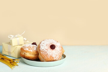 Plate with tasty donuts, gifts and candles for Hanukkah celebration on table against color background