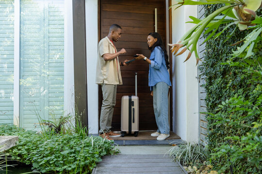 Presenting signature pad African American men holding smartphone on porch, with rolling suitcase