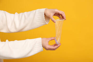 Female hands with open condom on yellow background, closeup