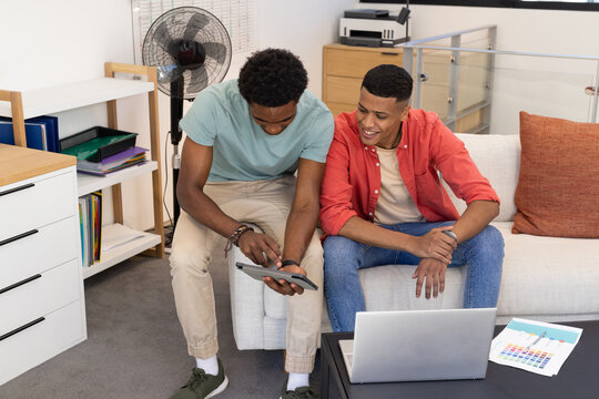 Tapping tablet, Diverse male friends working on sofa in home office, with laptop and color chart