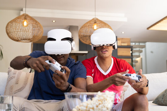 Playing VR games, Diverse male friends gaming in living room, holding white controllers and popcorn