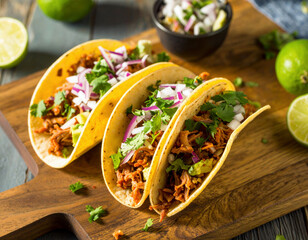 deliciously filled tacos sit on a rustic wooden plate, bursting with seasoned shredded meat, fresh cilantro, chopped onions, and vibrant flavors perfect for a festive meal.	