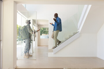African American father and son hugging in glass entryway, with son carrying military backpack
