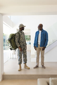 Standing African American father and son facing each other in home entryway, with military backpack