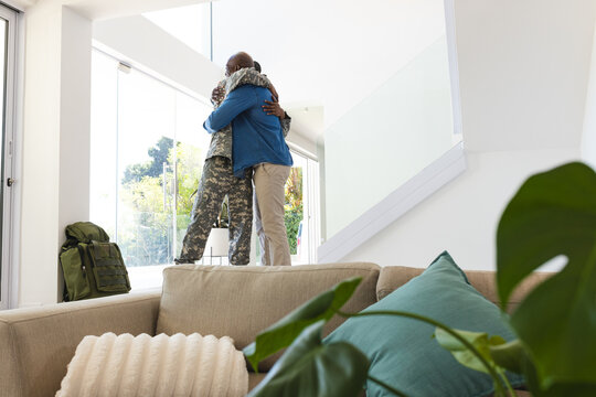 Embracing African American father and son standing by glass door at home, with military backpack