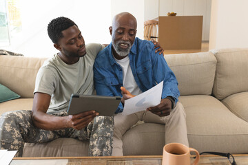 African American father and son studying documents on couch in living room, with tablet and charts