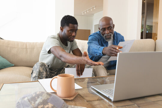 Examining documents and laptop in living room, African American father and son with military cap
