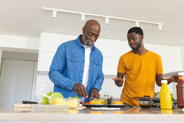 African American father and son assembling burgers on marble kitchen counter, with tomato, lettuce