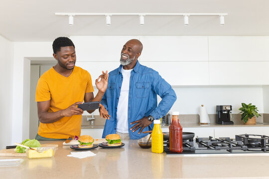 Cooking African American father and son preparing hamburgers in modern kitchen, using tablet device