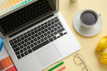 Workplace of graphic designer with laptop, coffee and color charts on yellow background
