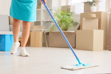 Female janitor mopping floor in room on moving day