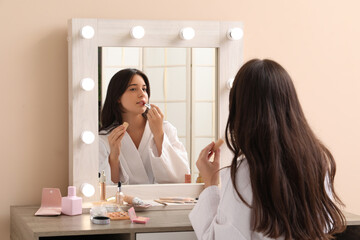 Young woman doing makeup at dressing table at home