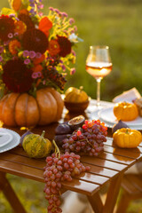 Beautiful elegant autumn table setting for thanksgiving family dinner or wedding. Orange pumpkin with flowers as centrepiece. Cozy fall home atmosphere. Wineglass, romantic marriage proposal, sunset
