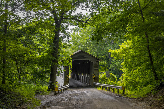 Historic State road covered bridge in Ashtabula county, Ohio surrounded with lush green foliage.