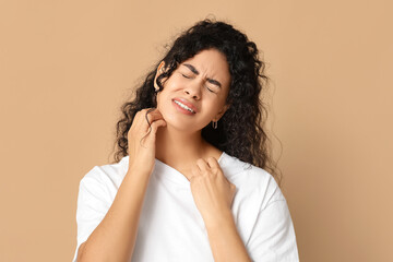 Young African-American woman suffering from skin allergy on beige background