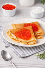 Delicious crepes topped with red caviar served on a cozy table setting in daylight
