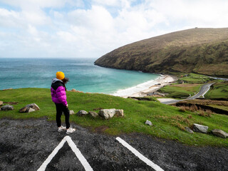 Teenager girl is looking at majestic nature scenery from car park. Keem bay and beach in county...