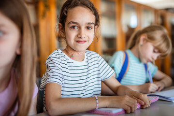 Portrait of little school girl with notebook in the school library