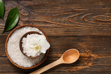 Composition with bowls of sea salt, orchid flower and spoon on wooden background