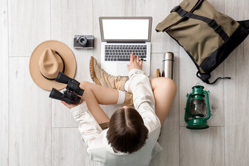 Female traveler using laptop with accessories on light wooden floor, top view