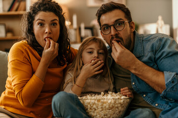 Family watching tv and eating popcorn on sofa