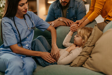 Female doctor examining little girl's abdomen at home with parents supporting