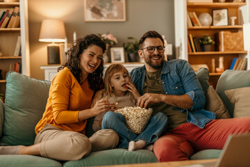 Happy family watching tv and eating popcorn on sofa at home