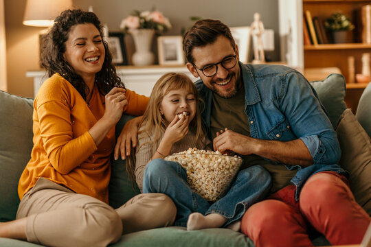 Happy family watching tv and eating popcorn on sofa at home