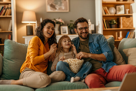 Happy family watching movie and eating popcorn on sofa