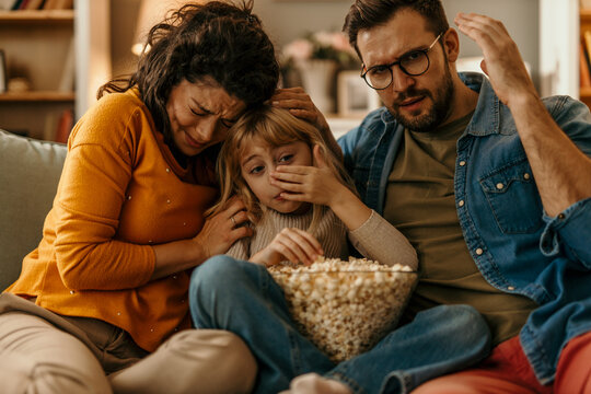 Family watching scary movie on tv, eating popcorn and feeling scared
