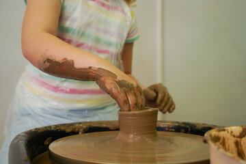 Child hands make earthenware cup working on pottery wheel at workshop.