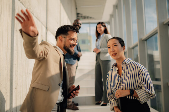Businessman showing something to his asian colleague in a modern office hallway