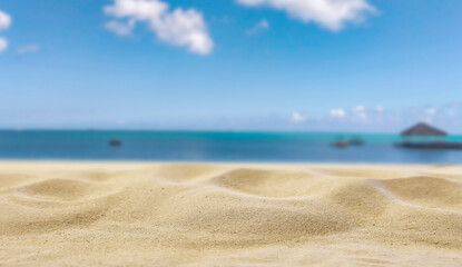 Beach Sand Close-Up with Copy Space – Summer Background for Product Placement. Sunlit beach sand with soft focus blue sea and sky in the background