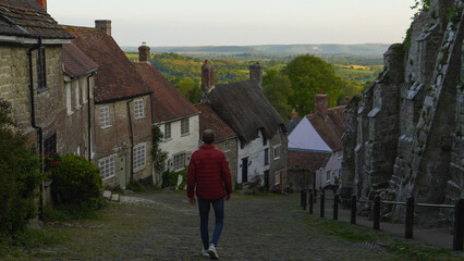 Person walking down a steep road through a charming village in England