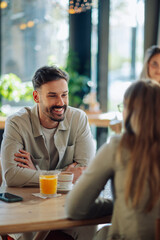 Happy man talking with woman in a cafe, enjoying coffee and orange juice