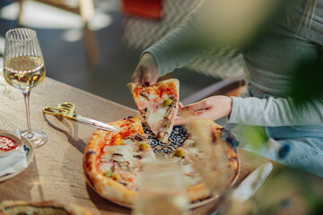 Woman picking up slice of pizza from decorative plate in restaurant