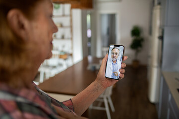 Senior woman having online video call with doctor at home using smartphone