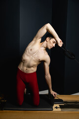 Slim male ballet dancer trains on Pilates equipment. Elegant pose, core strength, body control. 