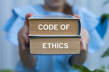 Young girl holding two books with inscription on side: CODE OF ETHICS. Code of ethics business...