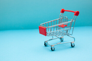Red shopping cart from supermarket on on blue background with copy space, buy and sale concept