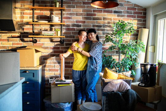 Portrait of a young smiling lesbian couple looking at camera after moving in their new home apartment