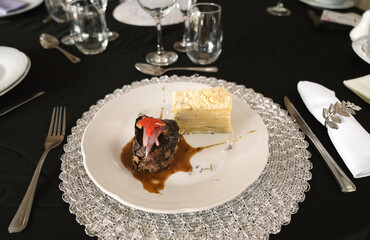 Gourmet gastronomy in a social event. Closeup view of a grilled loin fillet with sauce and a potato mille feuille in a white dish on the gala table with a beautiful tableware setting