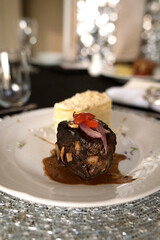 Gourmet gastronomy in a social event. Closeup view of a grilled loin fillet with sauce and a potato mille feuille in a white dish on the gala table