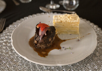Gourmet gastronomy in a social event. Closeup view of a grilled loin fillet with sauce and a potato mille feuille in a white dish on the gala table