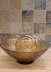 stylish glass bowl holds three elegant, textured spheres, all resting on light wooden surface. background features subtle, muted tiles that enhance contemporary aesthetic. close-up.