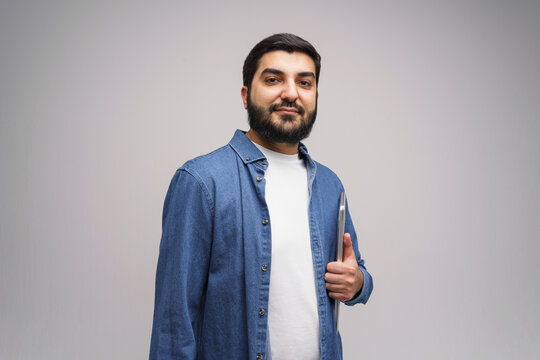Confident man in denim shirt giving a thumbs up while holding a tablet in a simple studio setting
