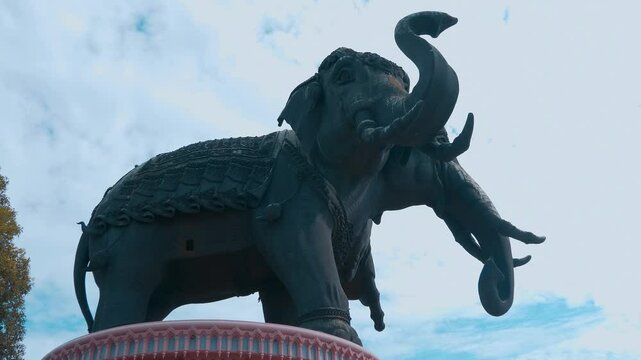 Colossal figure of the God Indra's vehicle - three headed elephant Erawan (Airavata) rises high above the ground against the blue sky in the Erawan Museum in Bangkok. Shot in motion