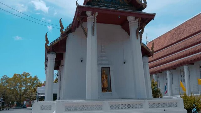 Buildings of Wat Na Phra Meru Rachikaram temple in Ayutthaya province, Thailand with its white walls and traditional Thai red tile roofs and gold carving and chofas. Shot in motion