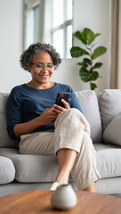 Obraz premium Smiling senior woman using smartphone on sofa at home